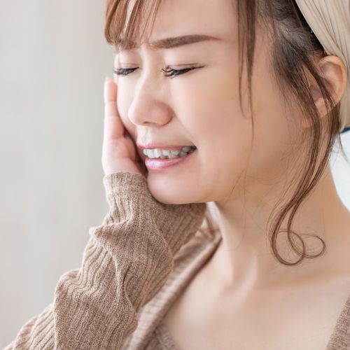 親知らずの炎症で痛みで頬を抑えている女性の画像